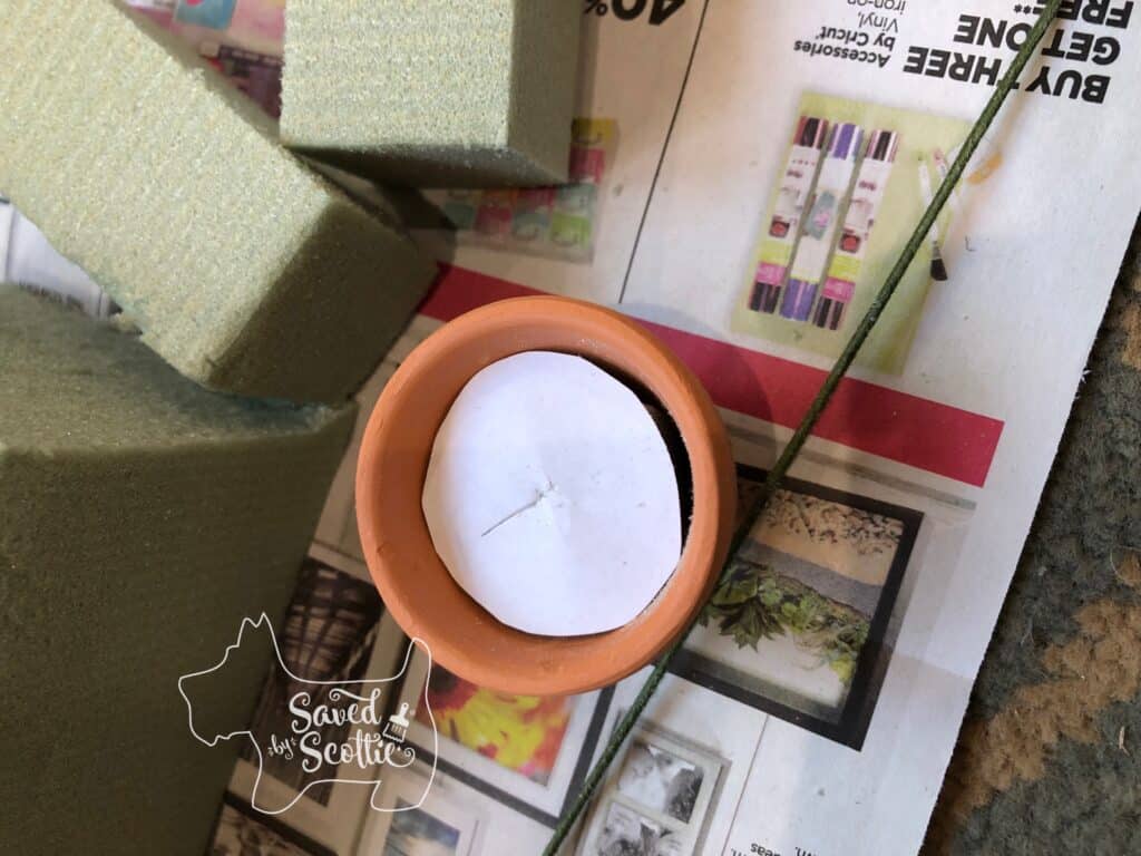 small terracotta pot with a piece of white paper cut to fill in the top next to cut blocks of floral foam on top of a colorful newspaper ad