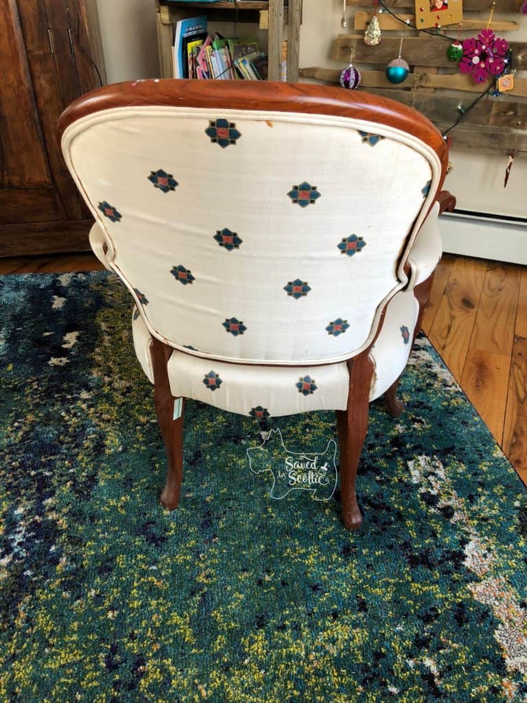 dated bergere arm chair needing to be reupholstered. in front of pallet christmas tree and fence board bookshelf. On wood floor and rug in teal and green tones. 