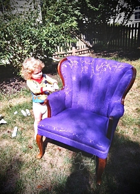 small child in toy story shirt examining chair for "missed spots". chair painted purple with wood legs and arms. 